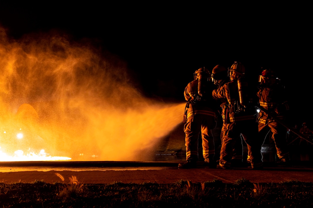 A group of Marines spray water on a large fire.