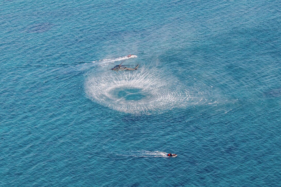 A helicopter hovers over a body of water as two small boats sail nearby.
