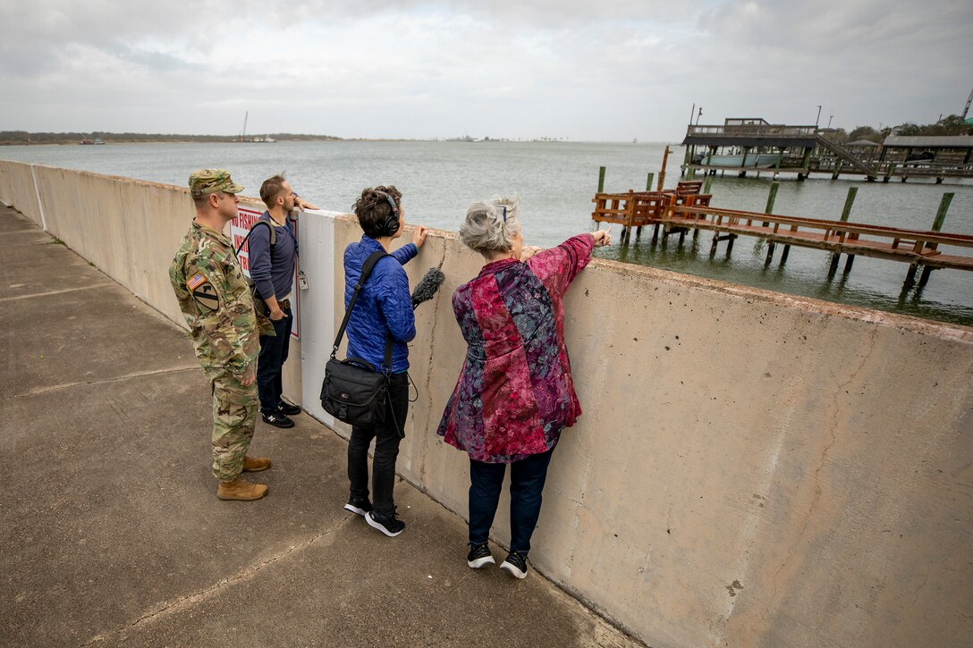 four people stand near a seawall in a fishing village area talking to each other.