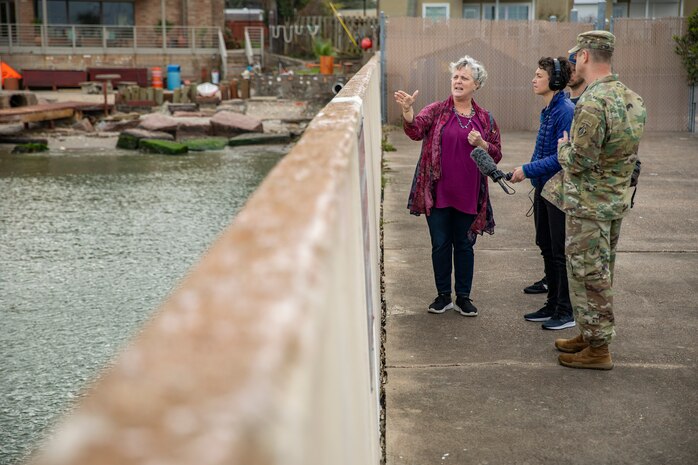 four people stand near a seawall in a fishing village area talking to each other.
