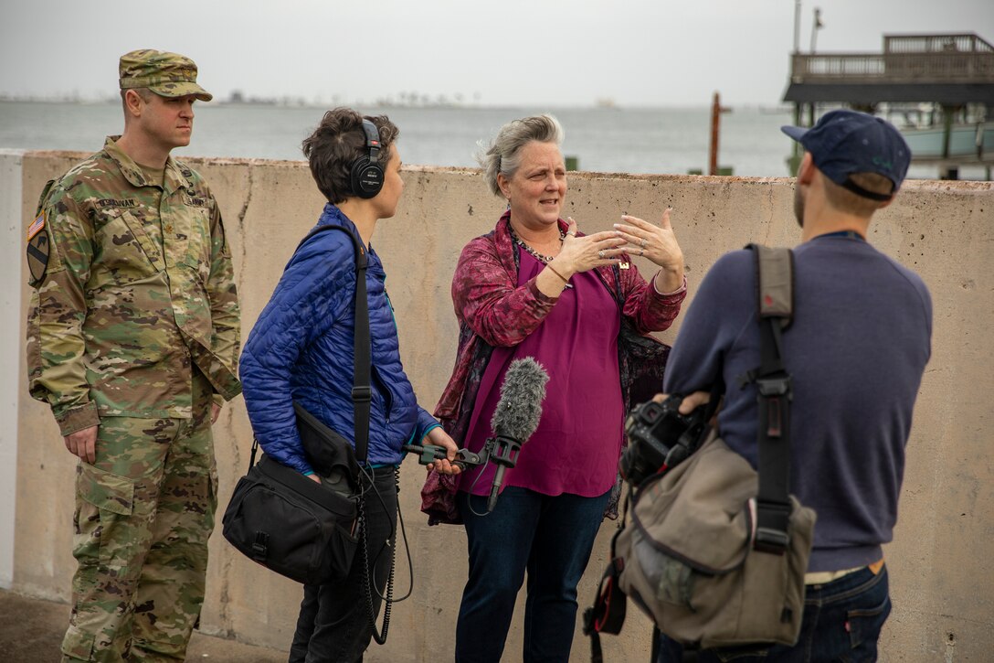 four people stand near a seawall in a fishing village area talking to each other.