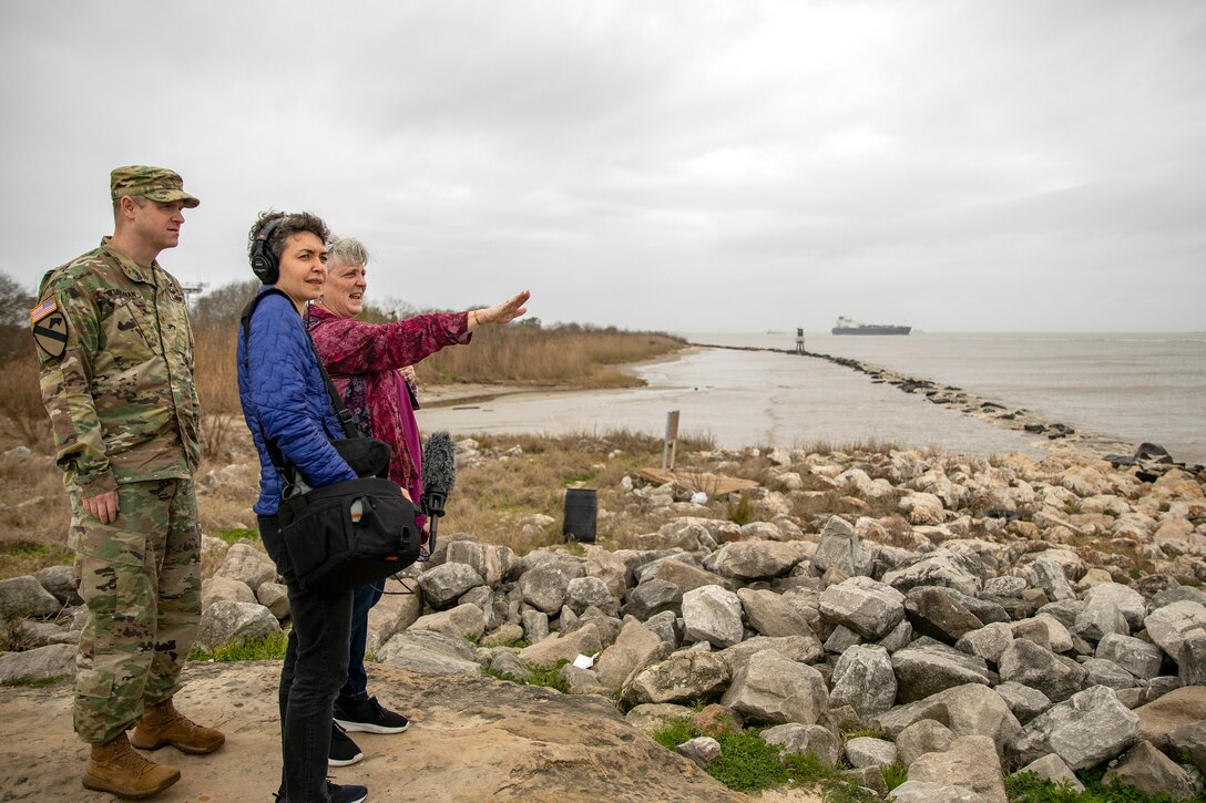 three people stand on a rocky ocean coastline talking to each other.