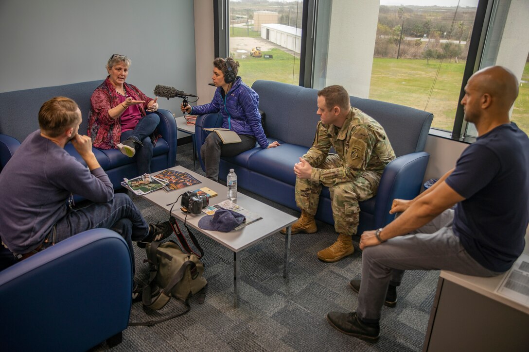 five people sit on couches and chairs in an office setting talking to each other.