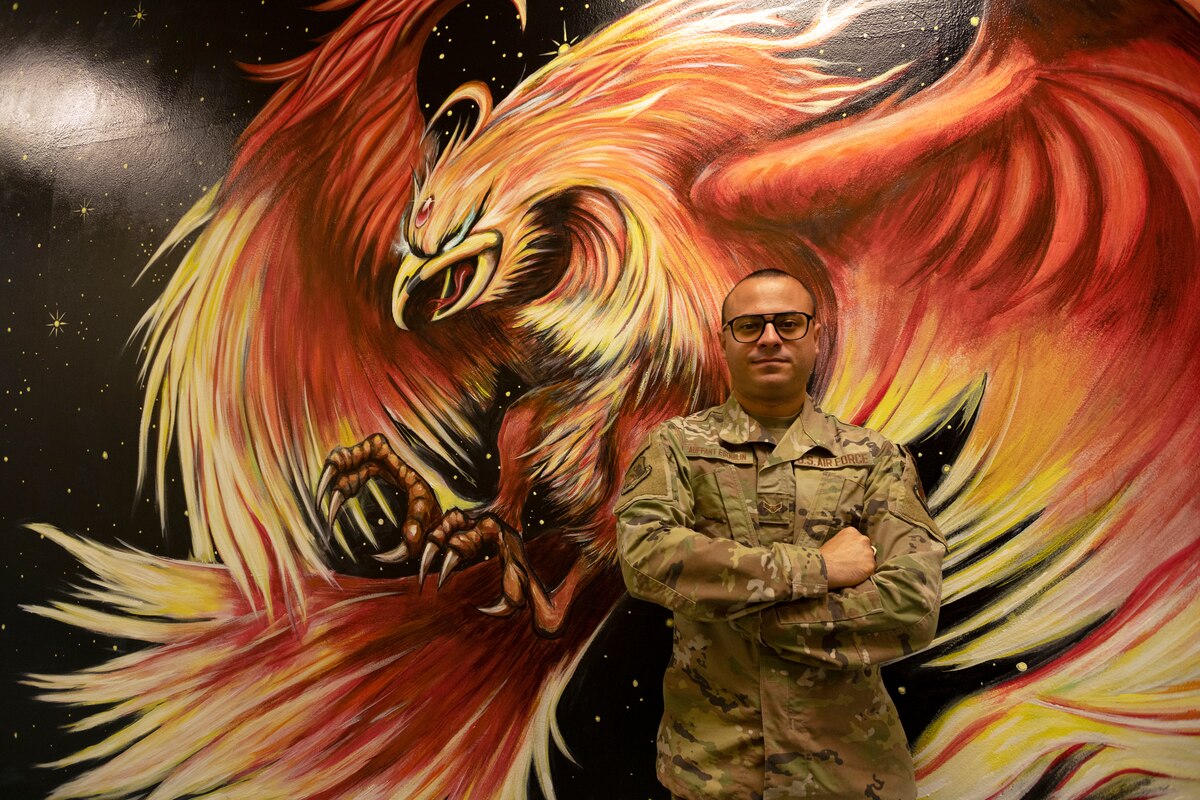 U.S. Air Force Airman 1st Class Alvin Auffant Esquilin, a cyber surety specialist with the 156th Combat Communications Squadron, poses in front of his mural of a phoenix in the squadron building at Muñiz Air National Guard Base, Feb. 4, 2023. As a talented artist, Auffant helped choose the phoenix, a mythical bird that arose out of its own ashes, as his squadron’s mascot for its associations with immortality, resurrection, resilience, uniqueness, and power. (U.S. Air National Guard photo by Airman 1st Class Marrissa L. Rodriguez)