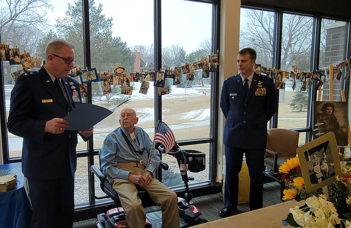 Two men in Air Force dress blue uniforms flank a man sitting on a motorized scooter