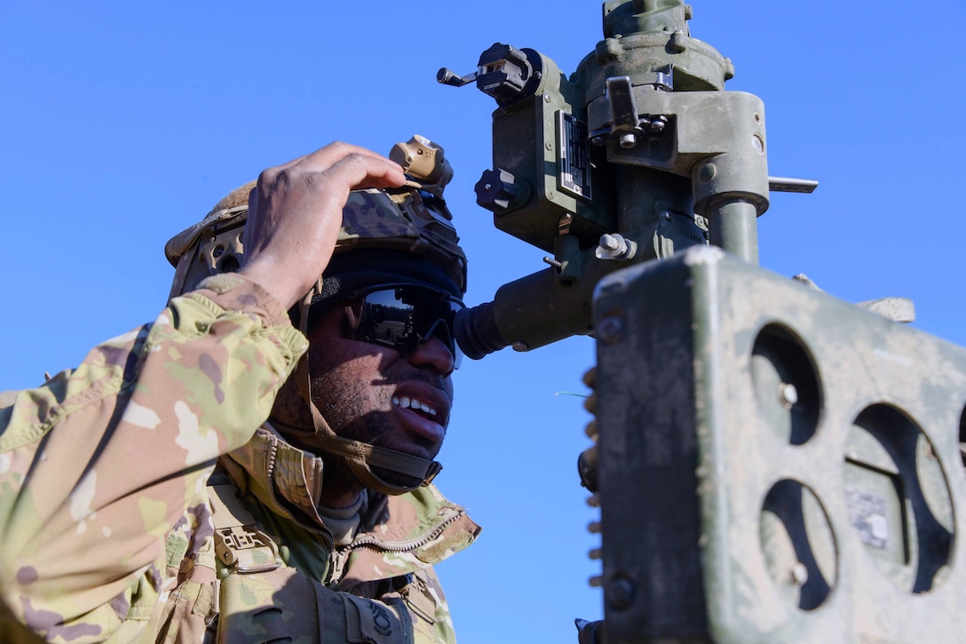 A soldier looks through the scope of a howitzer.