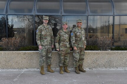 Three military members in uniform pose for a group photo