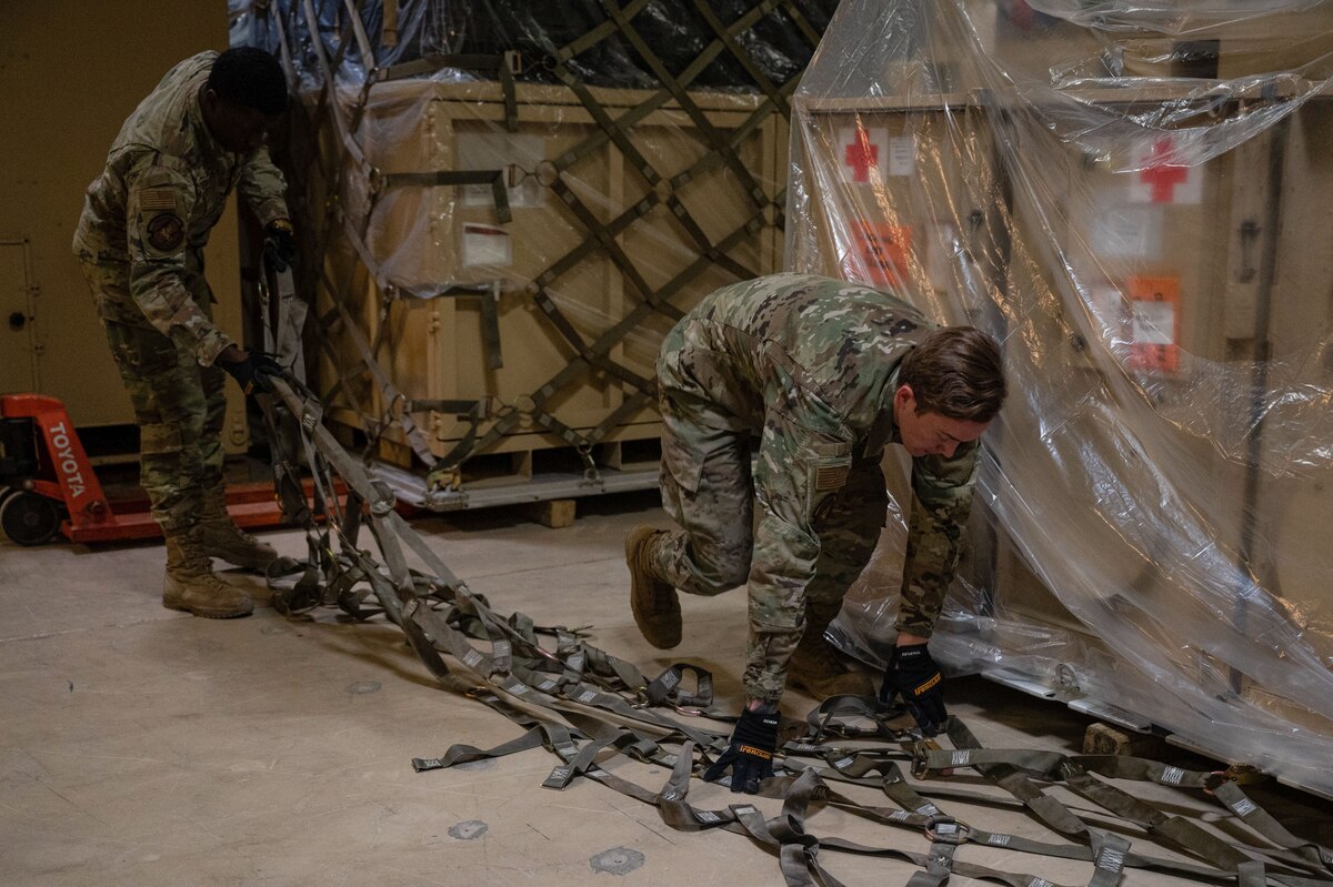 Airmen attach straps to pallets.