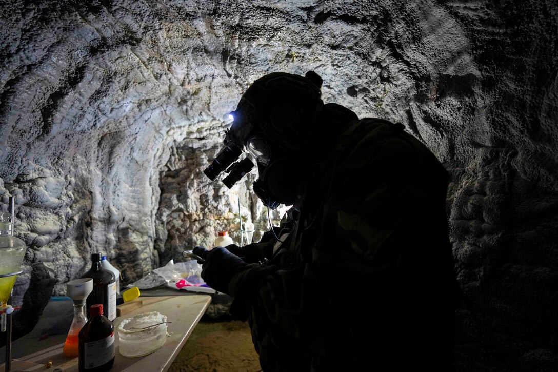 A soldier shown in silhouette conducts tests while wearing personal protective equipment.