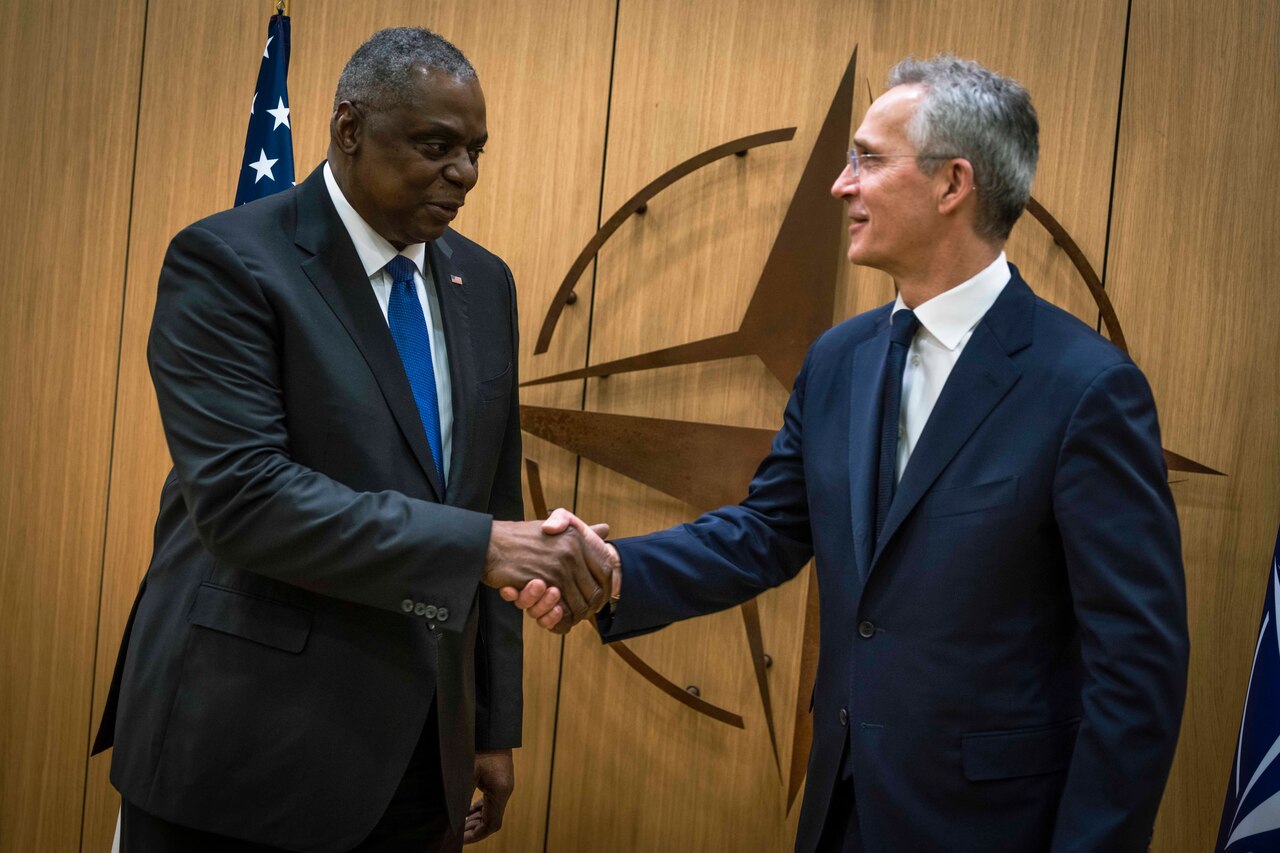 Two men shake hands and smile.