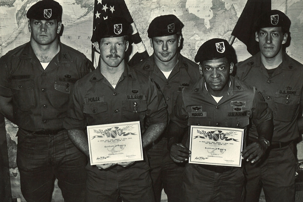 Five uniformed men wearing berets pose for a photo. Two hold up certificates.