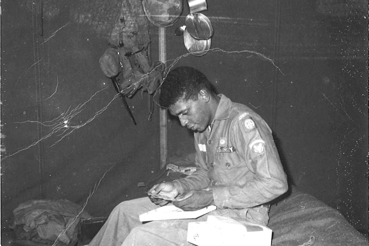 A man looks at an item from a box while sitting on a bed in what appears to be a canvas tent.