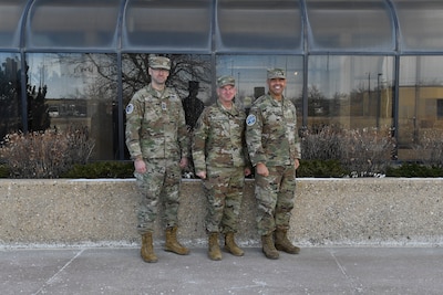 Three military members in uniform pose for a group photo