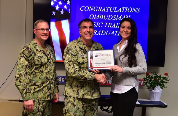 Naval Medical Forces Atlantic (NMFL) Command Master Chief Zachary Pryor and Rear Adm. Matthew Case, NMFL commander and director, Tidewater Market, present Emily Summers a certification of completion for the Ombudsman Basic Training (OBT) course, during a ceremony hosted by the Fleet and Family Support Center (FFSC) on board Joint Expeditionary Base Little-Creek Fort Story, Feb. 9, 2023.