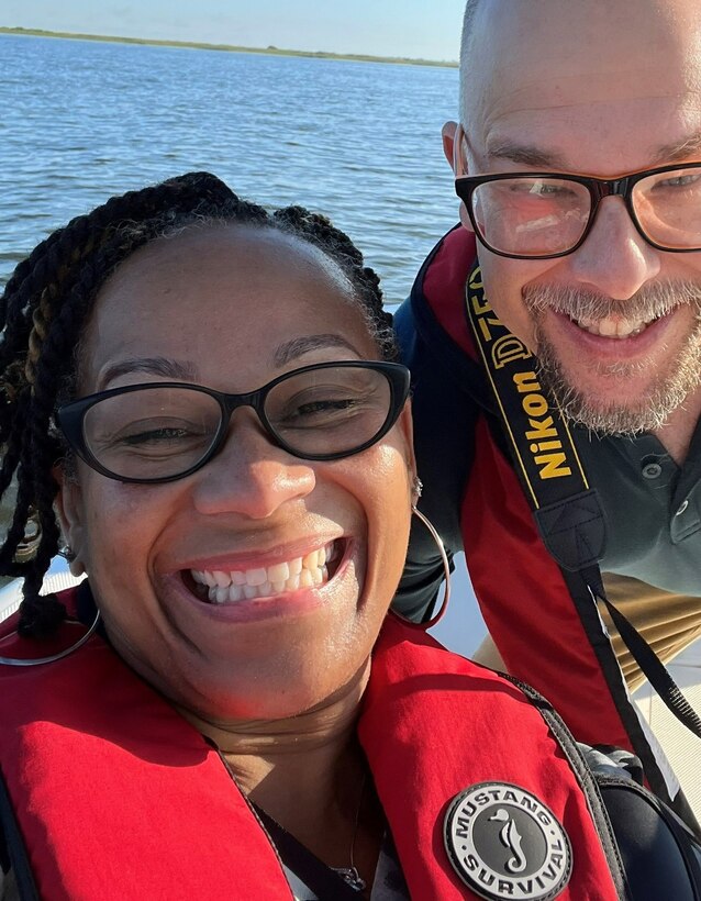 2 smiling people wearing red lifejackets with water in the background