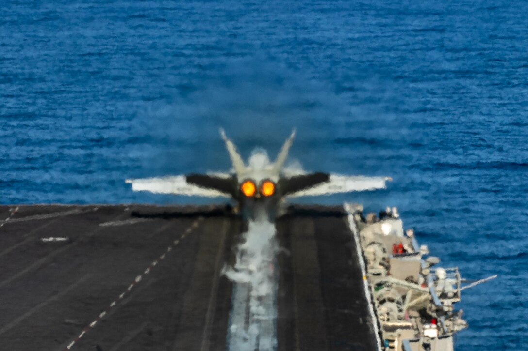 A military aircraft launches from the flight deck of a Navy ship.