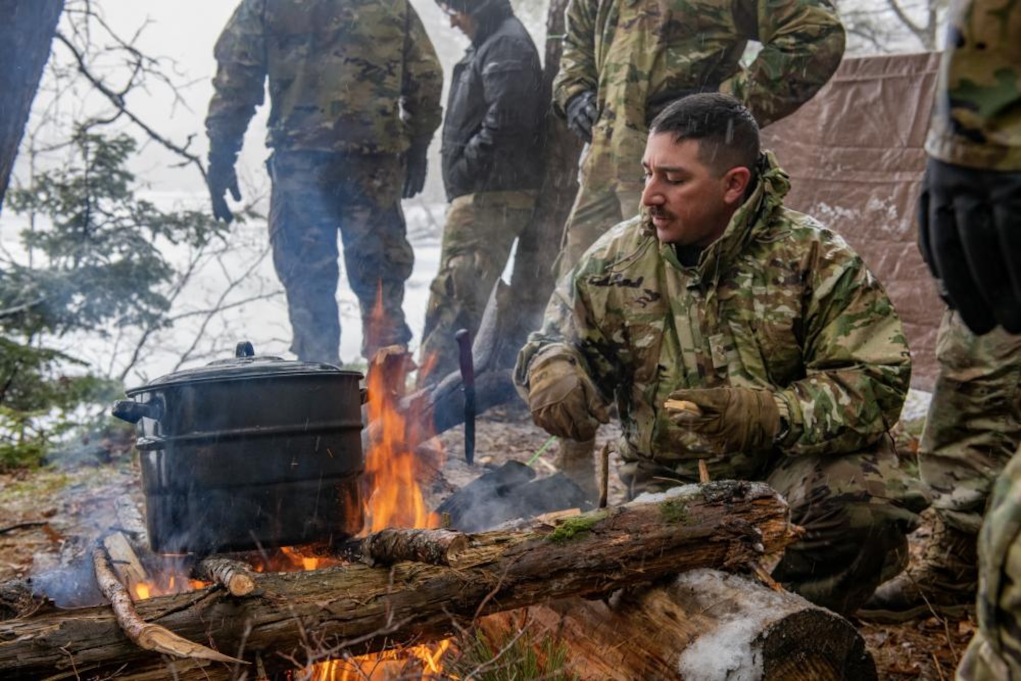 U.S. Air Force Senior Airman Louis Delgardio, of the 290th Joint Communications Support Squadron, boils water over a campfire Feb. 9, 2023, at Alpena Combat Readiness Training Center, Michigan. Airmen from the 290th are attending a class led by Survival, Evasion, Resistance and Escape (SERE) Specialists to teach them basic survival techniques in a cold weather environment. (U.S. Air National Guard photo by Senior Airman Jesse Hanson)