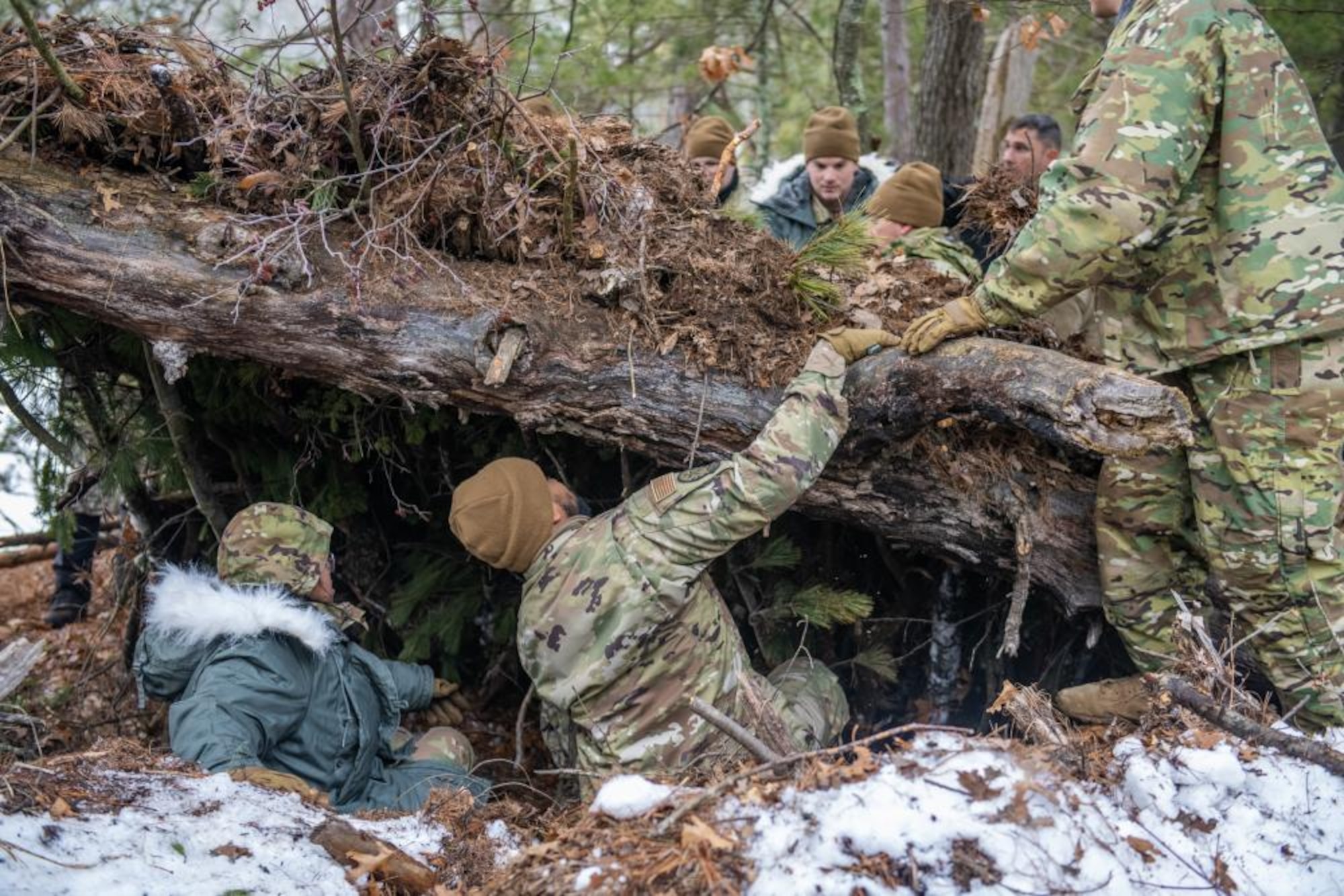 U.S. Air Force Airmen of the 290th Joint Communications Support Squadron assemble a natural shelter Feb. 9, 2023, at Alpena Combat Readiness Training Center, Michigan. The Airmen are attending a class led by Survival, Evasion, Resistance and Escape(SERE) specialists to teach them basic survival techniques in a cold weather environment. (U.S. Air National Guard photo by Senior Airman Jesse Hanson)
