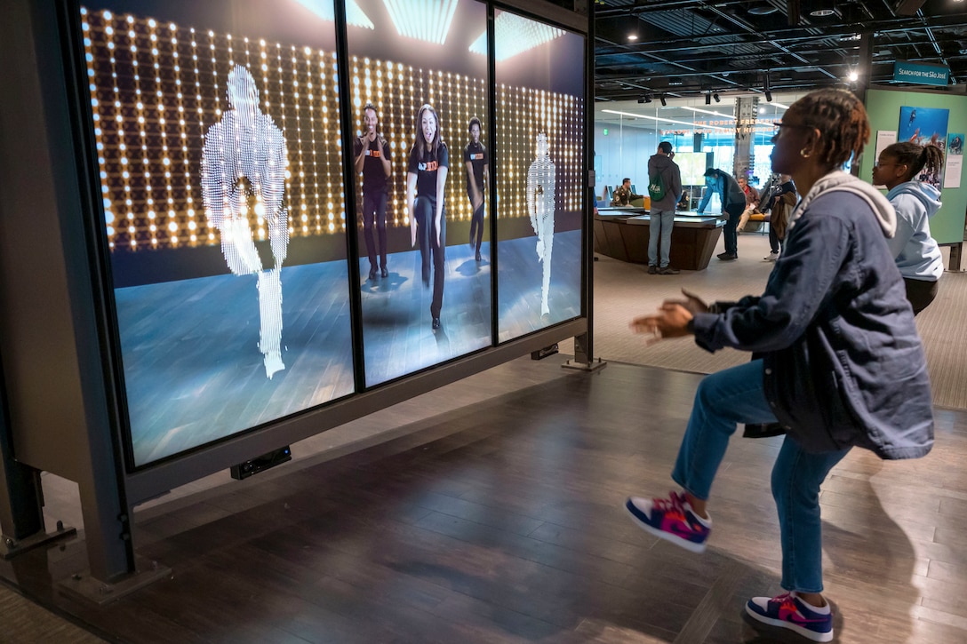 An airman dances with an interactive display at a museum.