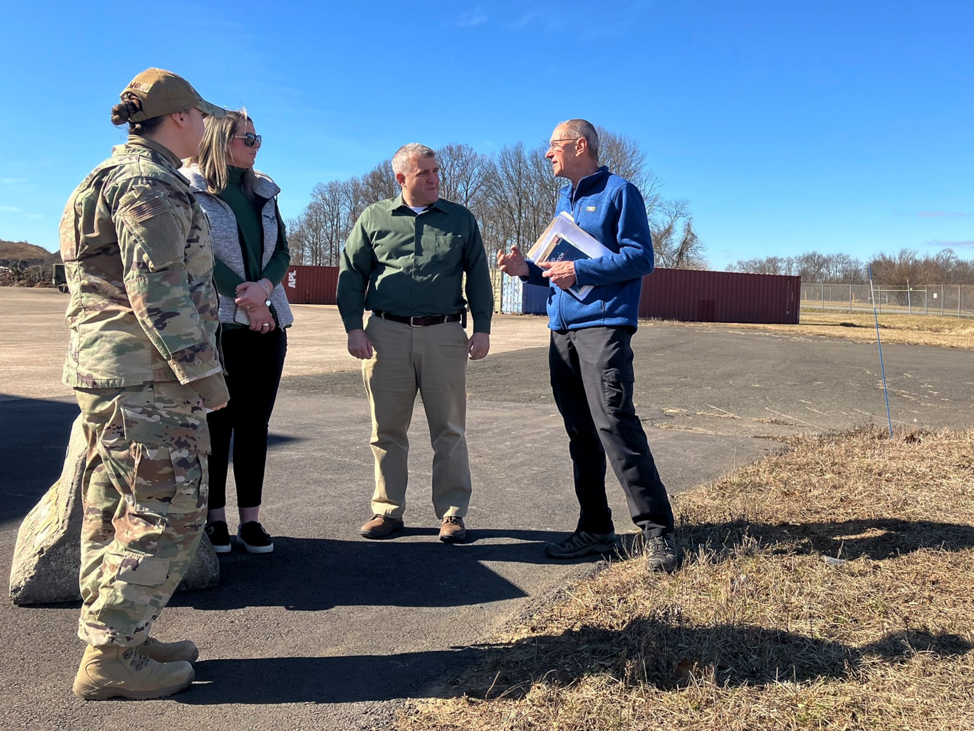 A group of people and a woman in military uniform stand outside and talk.