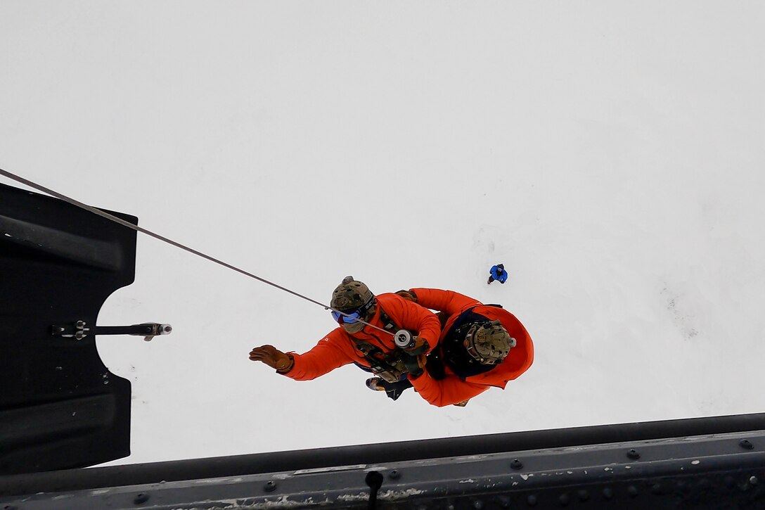 Two men are hoisted by a cable into a helicopter.