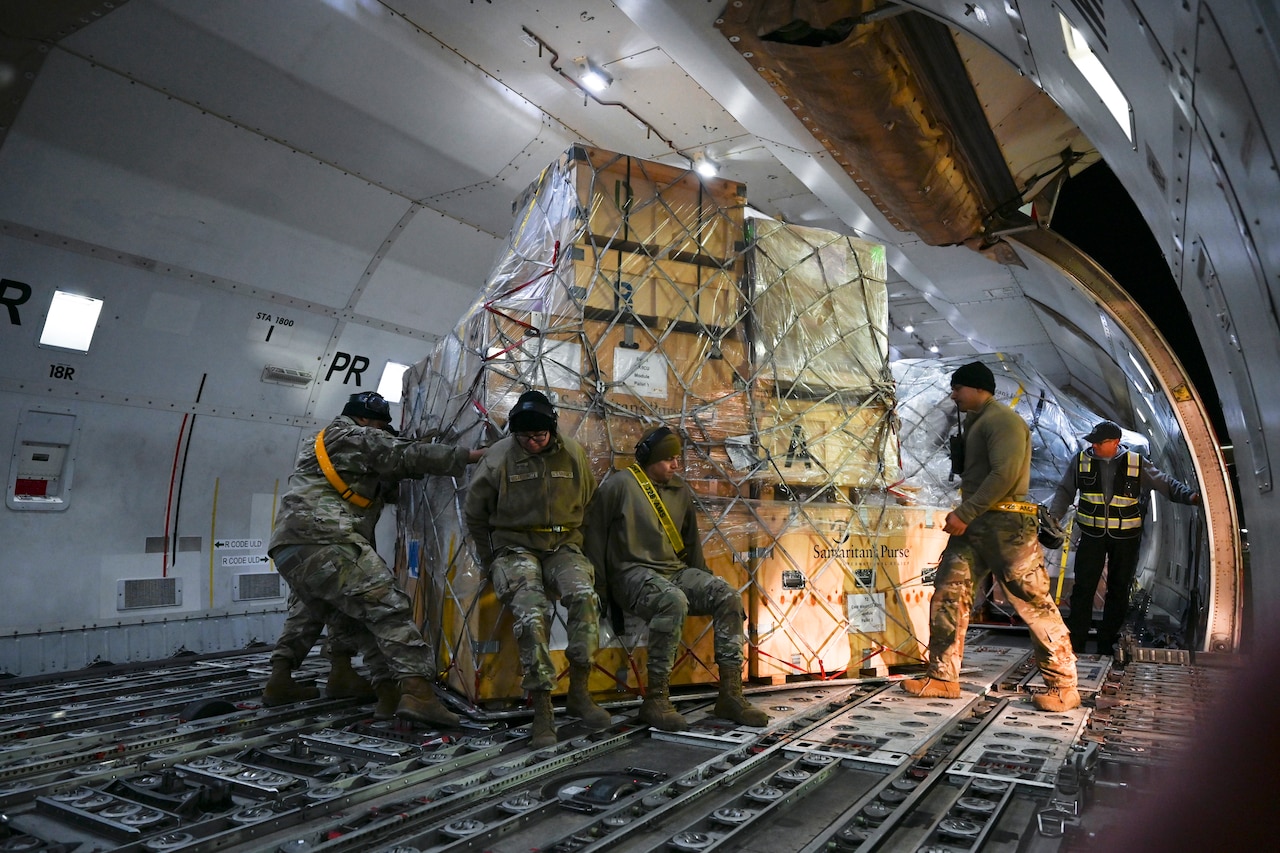 Airmen work to get a large pallet of supplies off an aircraft.