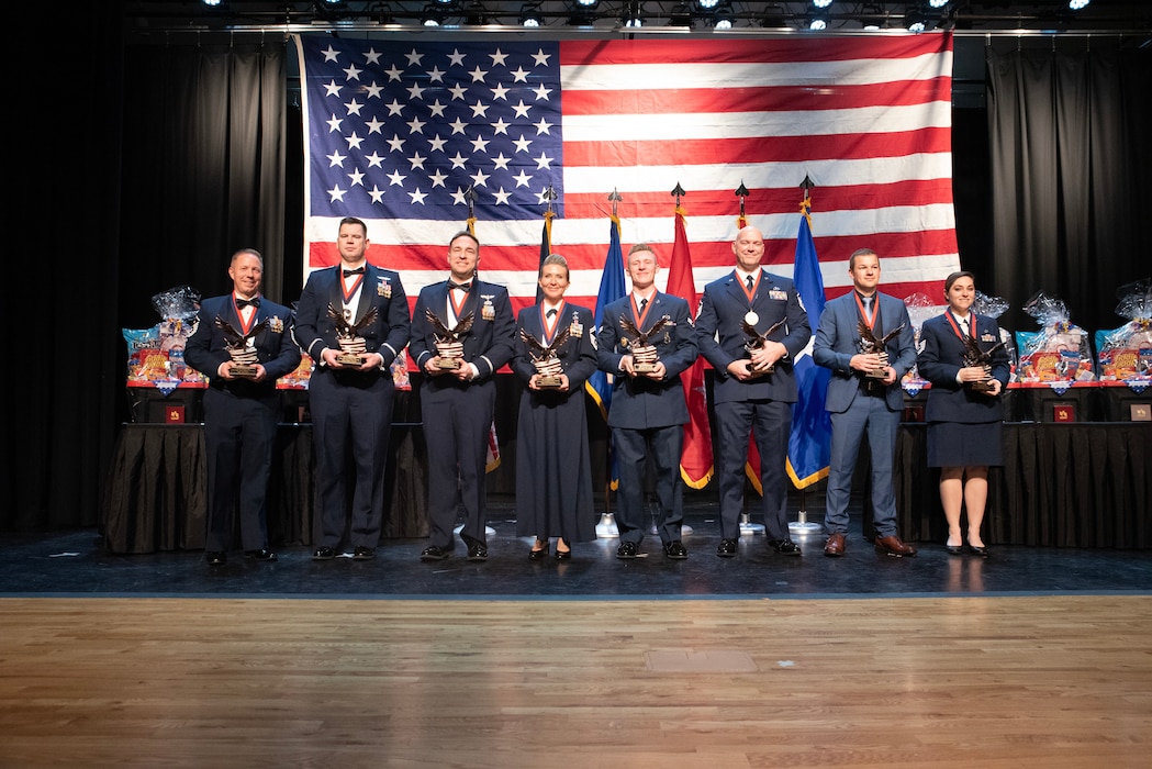 Service member stands on a stage holding their awards