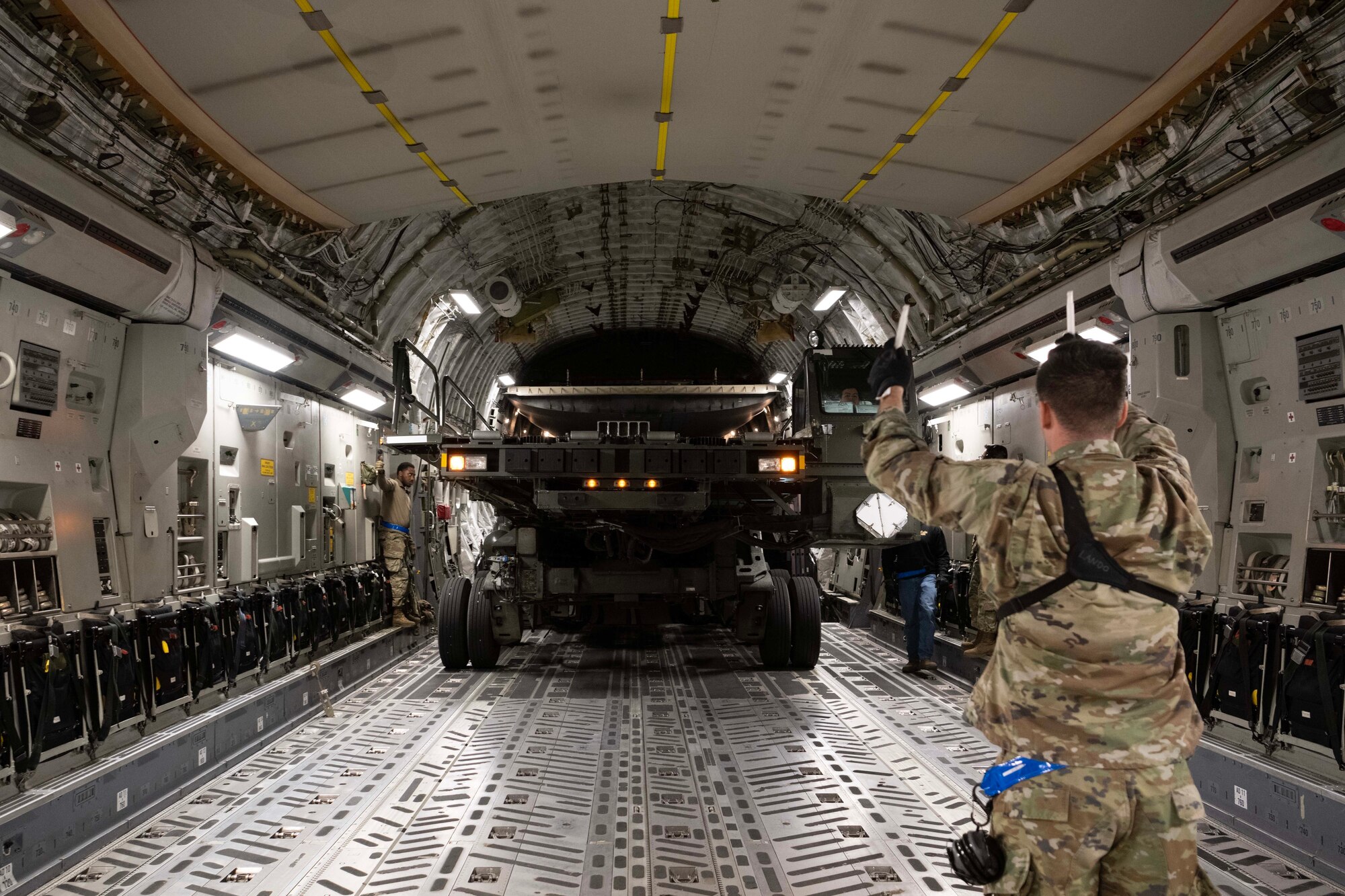 An Airman directs a large vehicle driven onto a plane