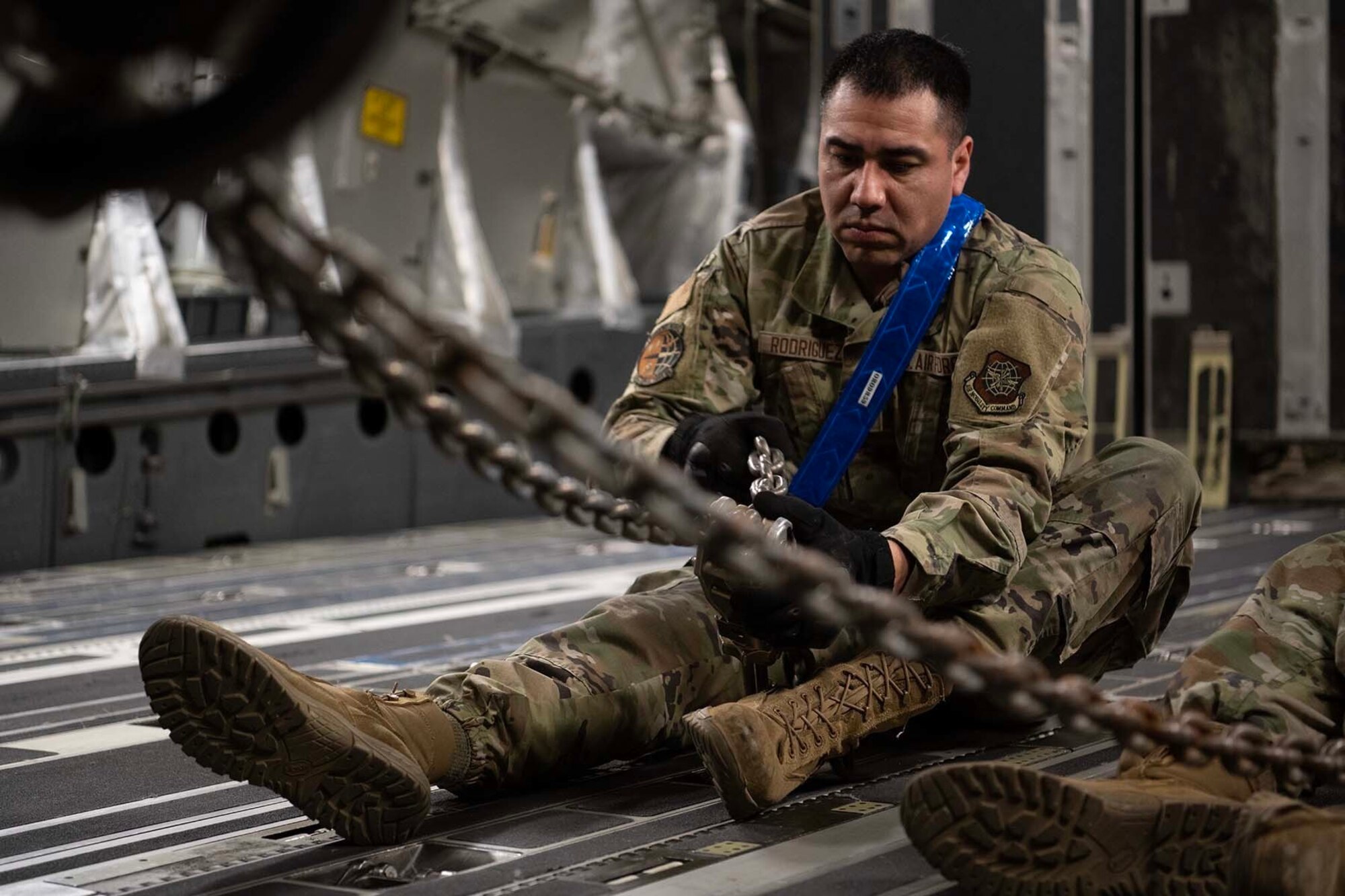 Airman sits on plane floor and locks a chain.