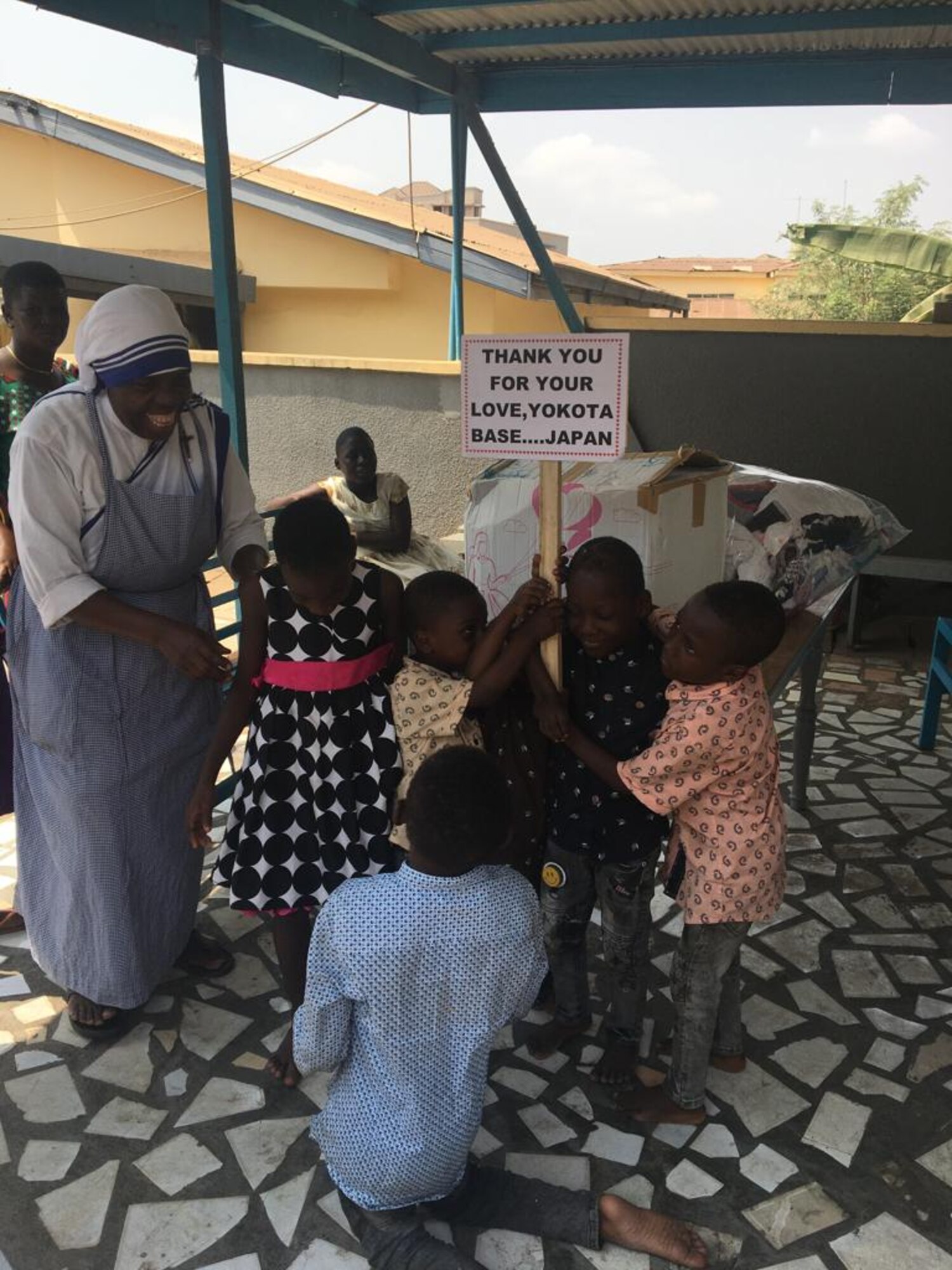 A nun from Ghana is surrounded by children holding a sign that thanks Yokota Air Base.