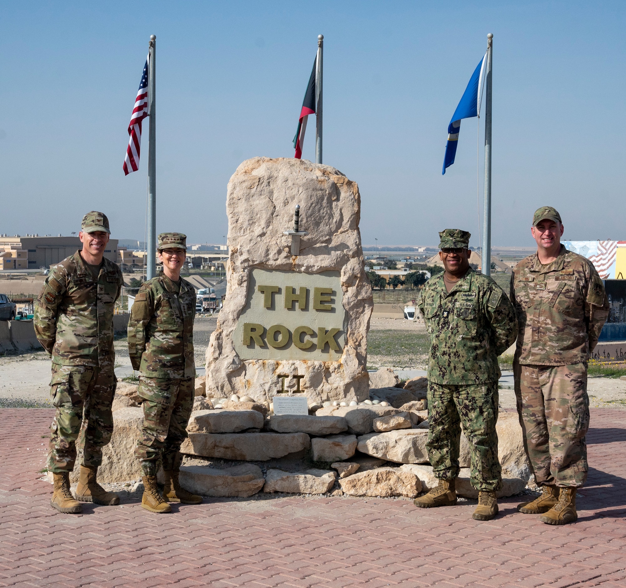 U.S. Air Force Gen. Jacqueline Van Ovost, U.S. Transportation Command commander, U.S. Navy Fleet Master Chief Petty Officer Donald O. Myrick, U.S. Transportation Command senior enlisted leader, Col. George Buch, 386th Air Expeditionary Wing commander, and Chief Master Sgt. Louis Ludwig, 386 AEW command chief, pose for a photo in front of "The Rock" at Ali Al Salem Air Base, Kuwait, Feb. 10, 2023.