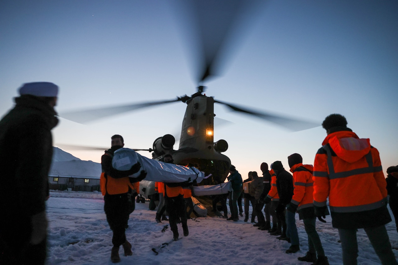 Two lines of soldiers and Turkish civilians offload humanitarian supplies from a helicopter.