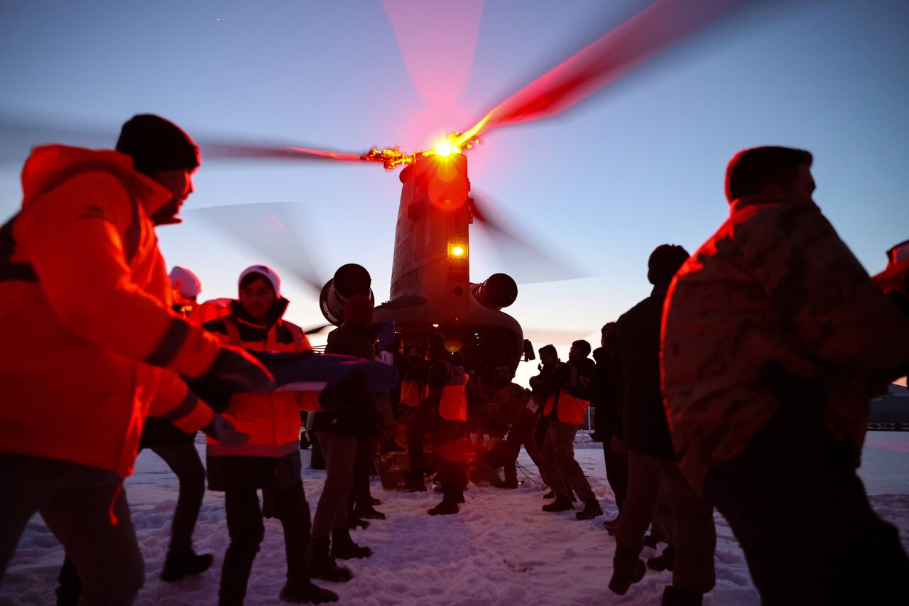 Two lines of soldiers and Turkish civilians offload a helicopter on snowy ground.