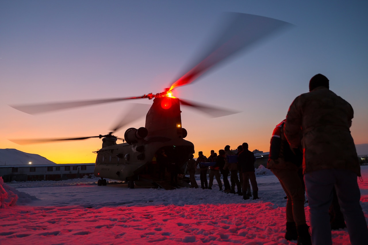 Soldiers and civilians offload boxes from a helicopter on snowy terrain.