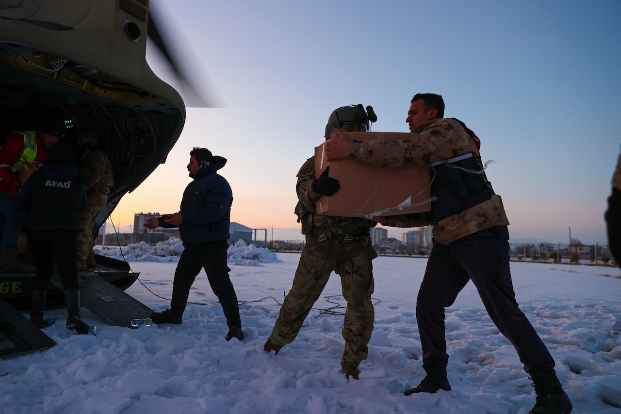 A soldier hands a package to a Turkish civilian while offloading humanitarian aid from a CH-47 Chinook helicopter.