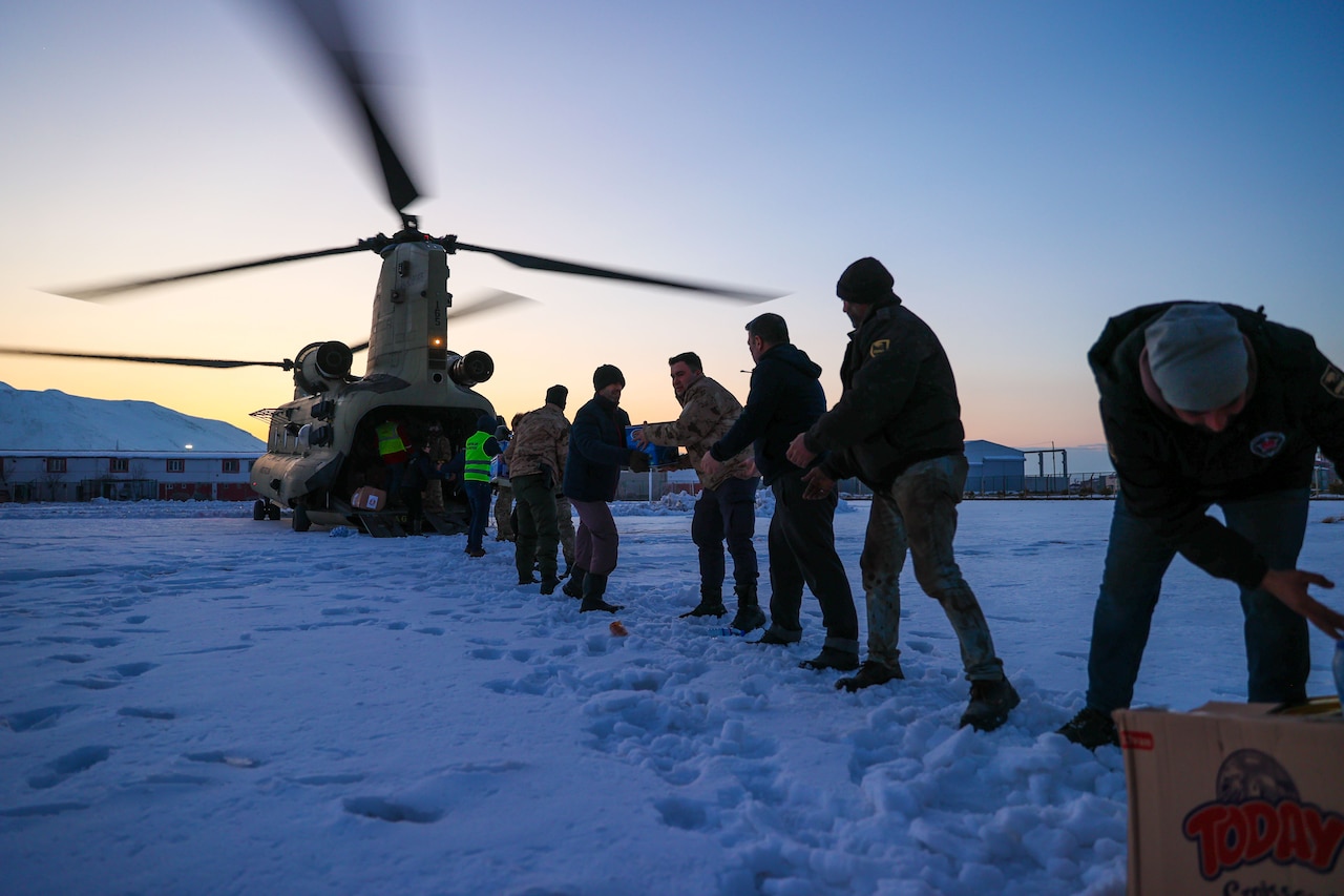 A line of soldiers and civilians unload packages from a helicopter.