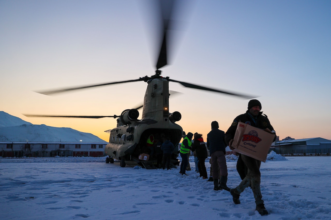 Soldiers and civilians carry boxes away from a helicopter in a line.