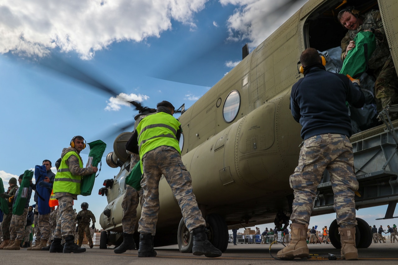 A line of service members load cargo onto a helicopter.