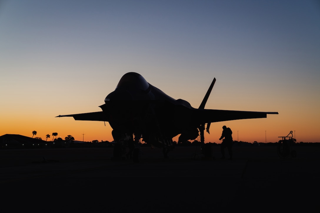 An airman walks below a large military aircraft at twilight.