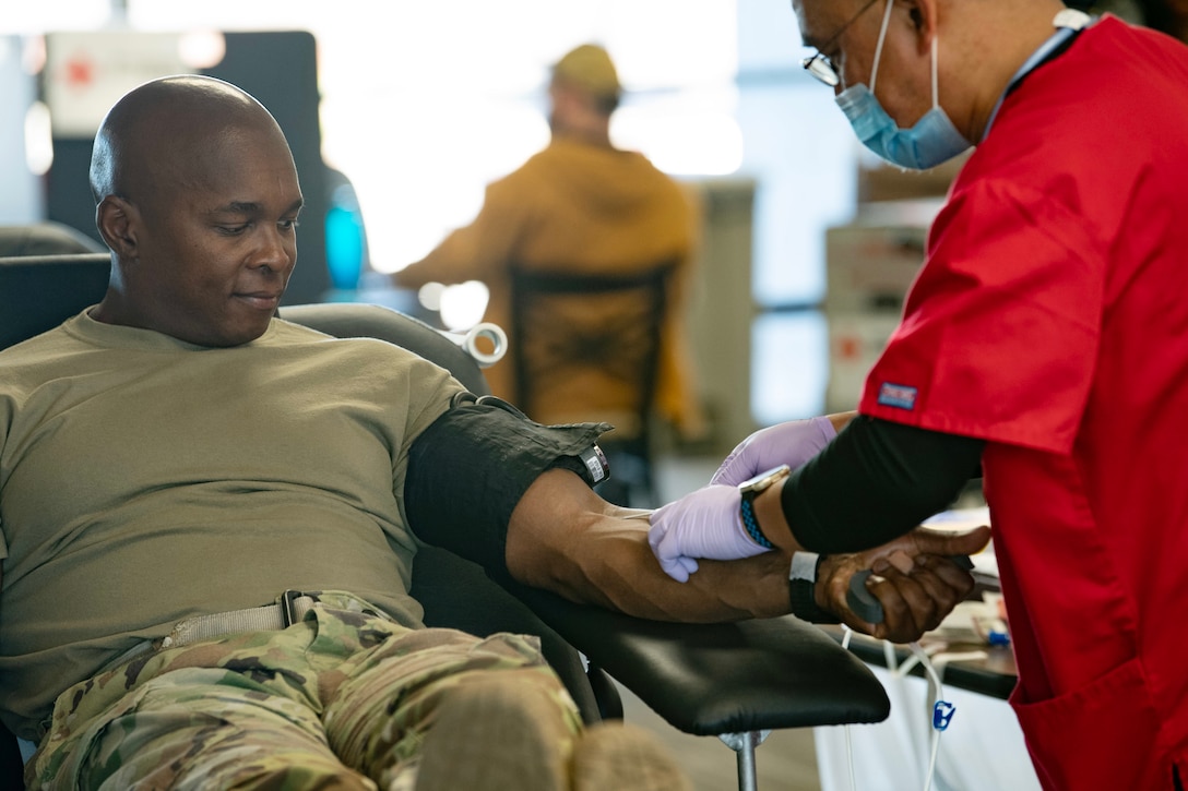 A soldier lies in a chair as a technician draws blood from his arm.
