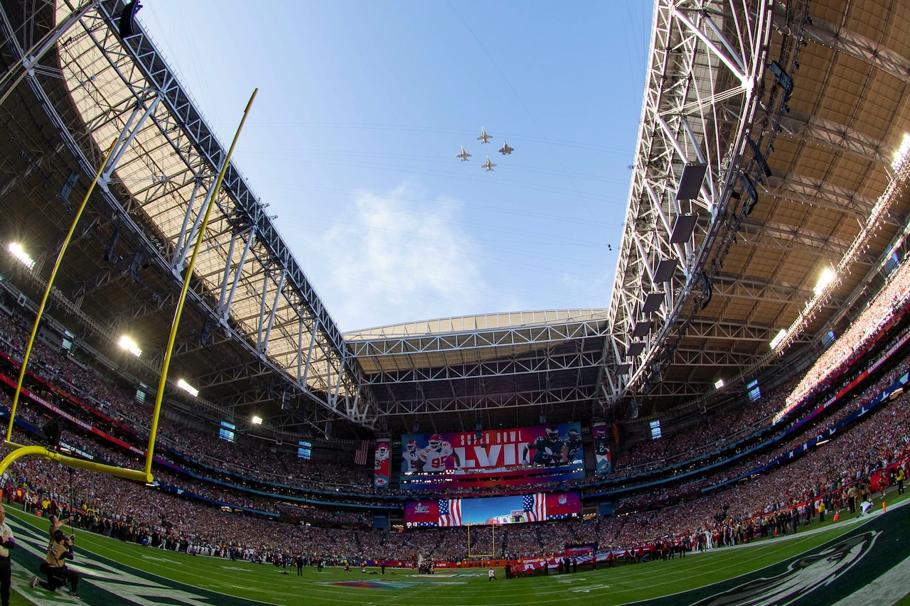 Four aircraft fly over a football stadium.