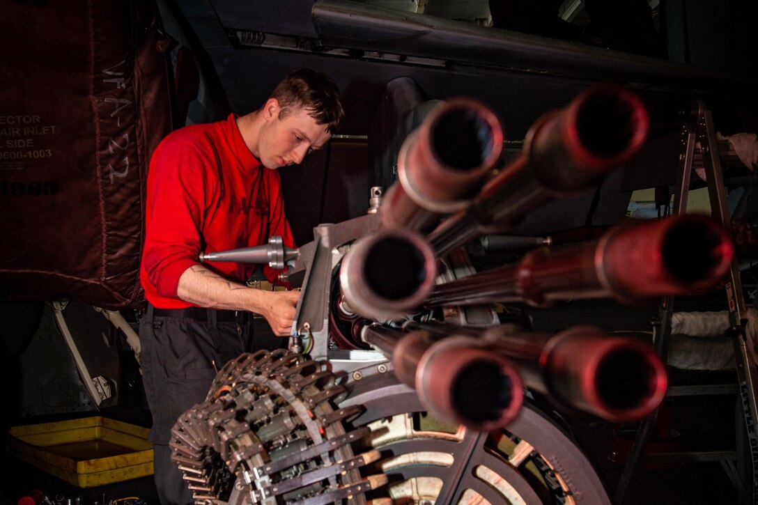 A sailor examines parts on a large gun.