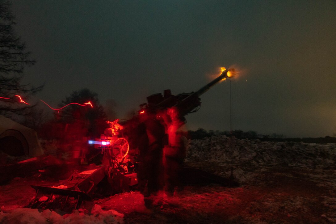 Marines, illuminated by a red light, fire artillery at night.