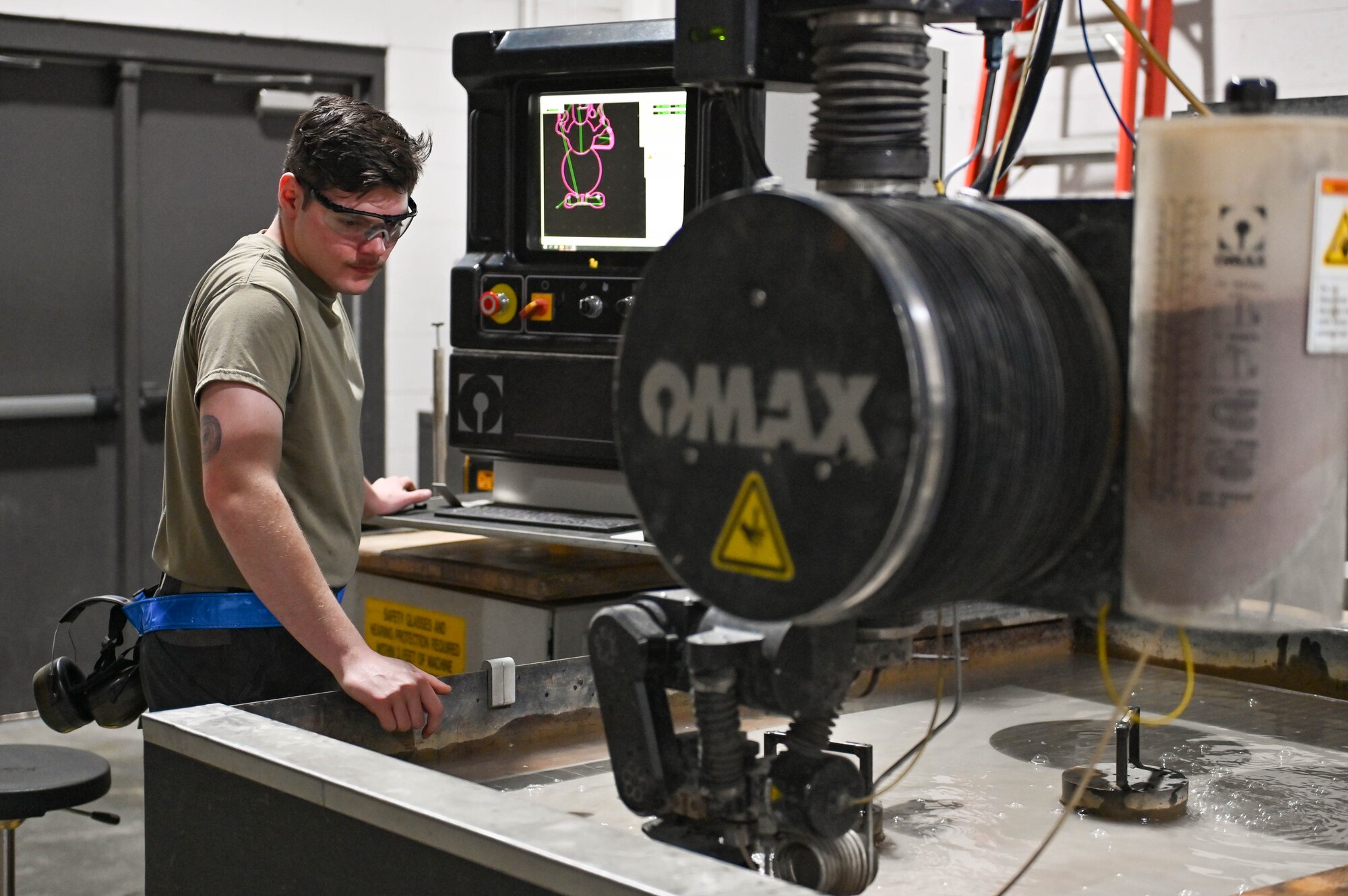 U.S. Air Force Airman 1st Class Broden Eckstein, 23rd Maintenance Squadron aircraft metals technician, uses a waterjet to cut a sheet of metal at Moody Air Force Base, Georgia, Dec. 13, 2022. The water jet can cut hard and soft materials into usable parts on aircraft or machinery. (U.S. Air Force photo Senior Airman Rebeckah Medeiros)