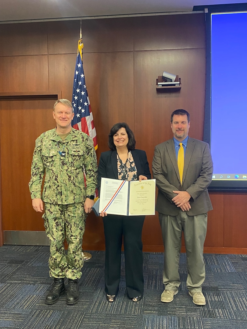 The Arleigh Burke Class (DDG 51) Destroyer Shipbuilding Program Manager Capt. Seth Miller (left) and Naval Sea Systems Flight (FLT) III Upgrade Manager PMS 400D Michael Dugan (right) present the Navy Meritorious Civilian Service Award to Toni Checchio, a Naval Surface Warfare Center, Philadelphia Division electrical engineer, for her performance throughout her 39-year career on Jan. 18, 2022 in Philadelphia. Checchio began working at NSWCPD in 1983 as a co-op, and she is set to retire on Feb. 28, 2023.