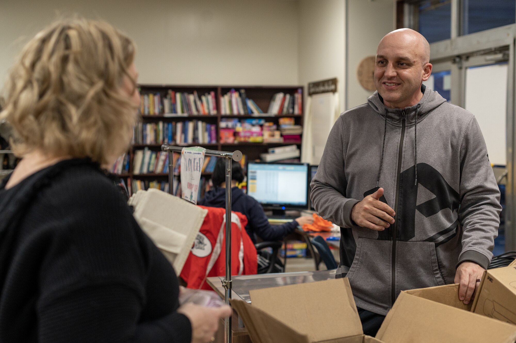 A bald man speaks with a woman in a thrift store.