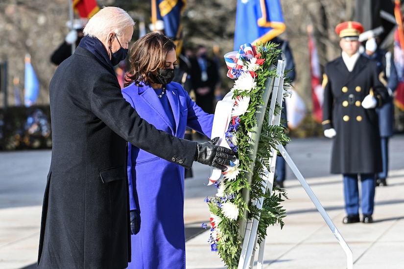 President Joe Biden and Vice President Kamala Harris place a wreath with a military guard and flags in the background.