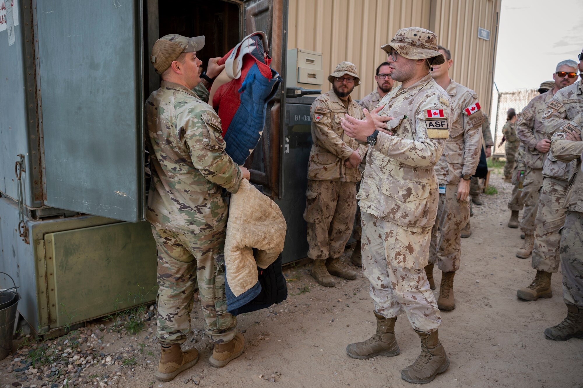 U.S. Air Force Tech. Sgt. Brendan Turner, 386th Expeditionary Security Forces Squadron kennel master, hands Cpl. Isaiah Coles, a Canadian Armed Forces member, a bite suit during a Military Working Dog bite demonstration at Ali Al Salem Air Base, Kuwait, Feb. 16, 2023.