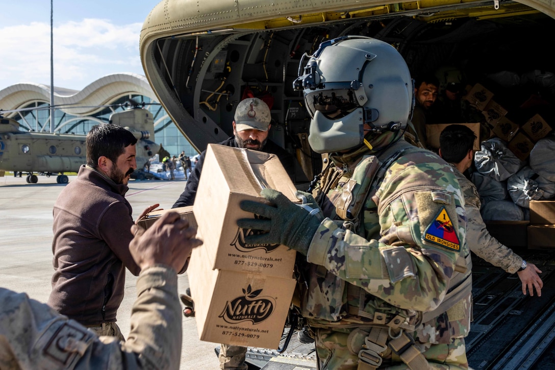 A soldier wearing full military gear helps delivers humanitarian aid supplies along with other soldiers and civilians.