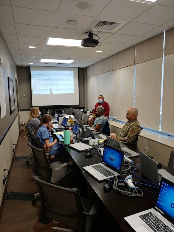 Military and civilians sit at a table with laptops during a meeting.